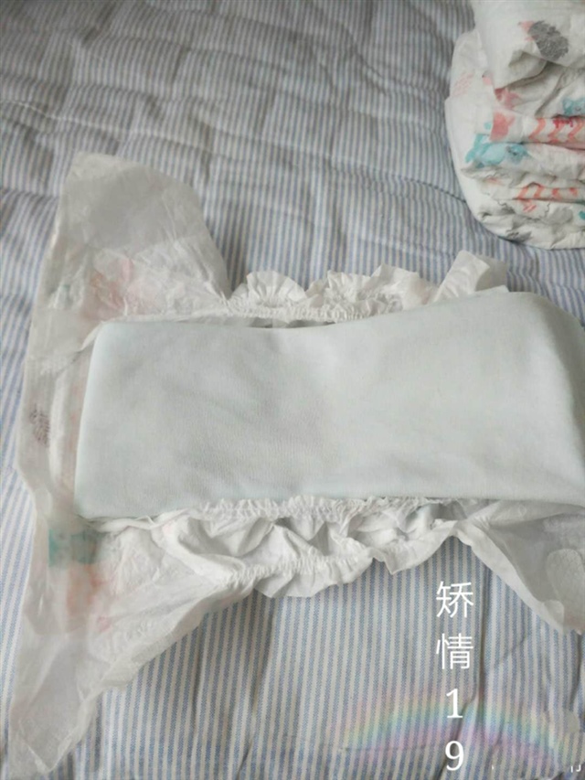 4.将叠好的尿布放进去，前面的部分对齐，用手按着另一只手将后面腰松紧部分拉开，将尿布放进兜里平铺。