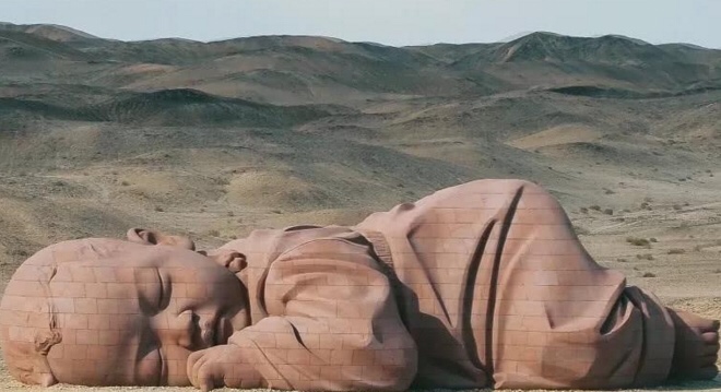 巨婴双眸轻轻闭上，就像是在沉睡一样，神态乖巧懂事。让人们忍不住的去仔细的观赏，不少女游客看到之后，都难免泛滥出喜爱之情，看到又是自己孤独的躺在沙漠里面，人人心疼而又感到神秘。